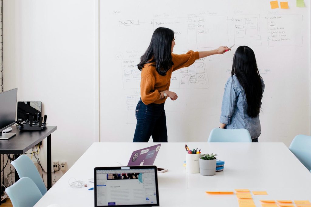 Two people planning work on whiteboard with laptops and sticky notes