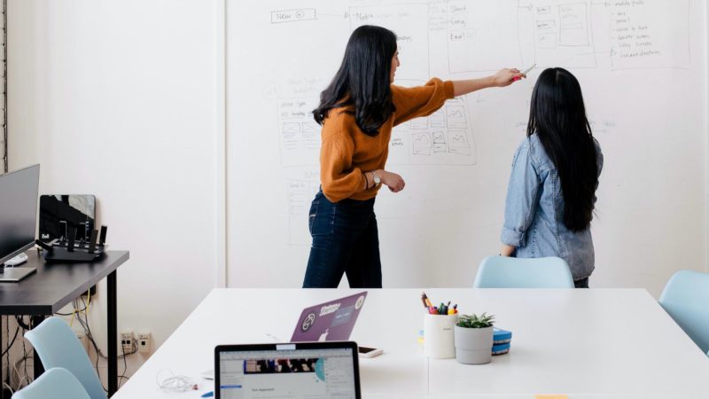 Two people planning work on whiteboard with laptops and sticky notes