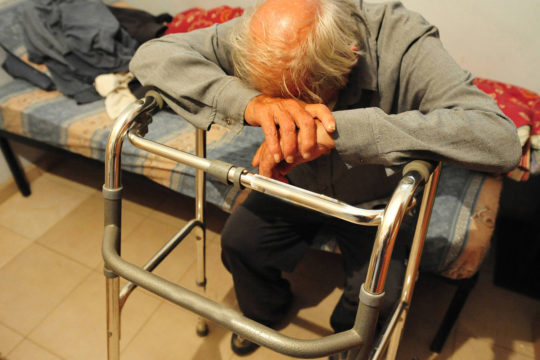 elderly man sitting alone on his bed.