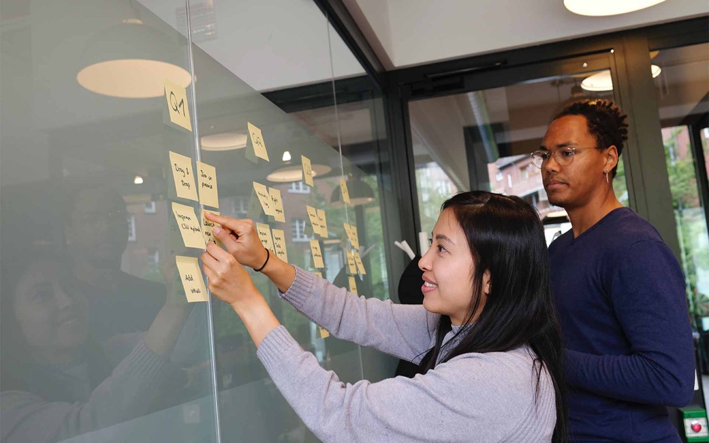 two people creating a process with post it notes stuck on a glass wall