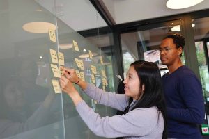 two people creating a process with post it notes stuck on a glass wall