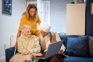 Older couple using laptop, younger female supervising, all smiling. CREDIT: Peter Kindersley