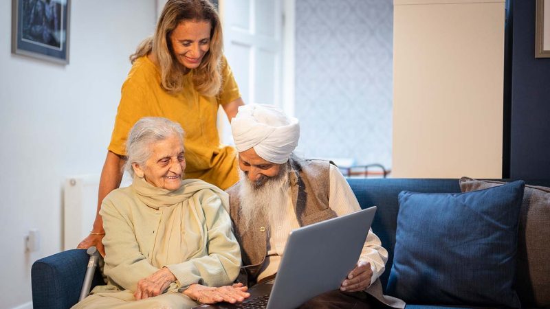 Older couple using laptop, younger female supervising, all smiling. CREDIT: Peter Kindersley