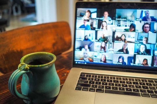Laptop open with blurred online meeting attendees. Cup next to Laptop.