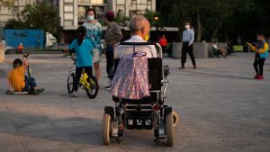 Older person sitting in mobility scooter looking at people walking and playing in the distance, Photo by Red John on Unsplash