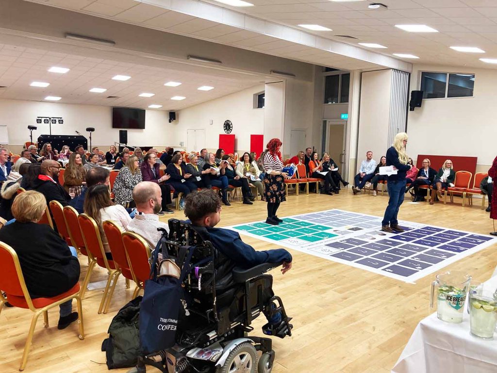 People playing giant boardgame. People sitting in chairs around large board game on the floor.