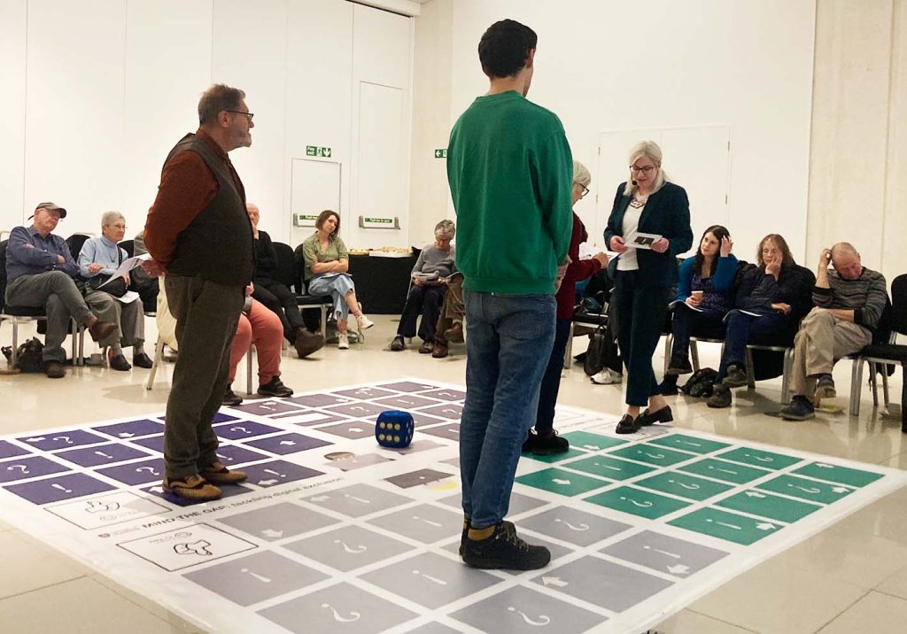 People playing giant boardgame. People sitting in chairs around large board game on the floor.