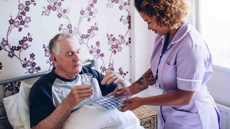 Member of care home staff helping patient with medication