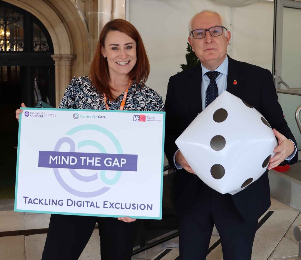 People smiling holding dice and Duncan Jordan MP holding board which says 'Mind the Gap: Tackling Digital Exclusion'