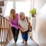 person helping older person climb stairs in house