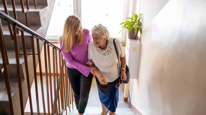 person helping older person climb stairs in house