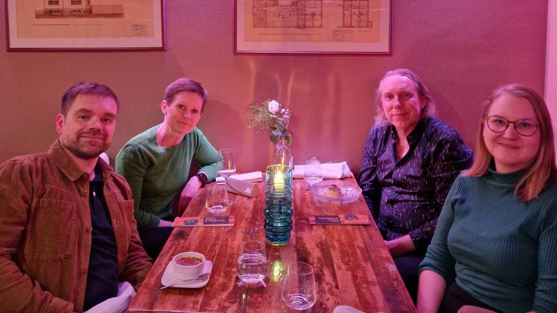 Four people sitting at a dining table in a room lit by purple lighting
