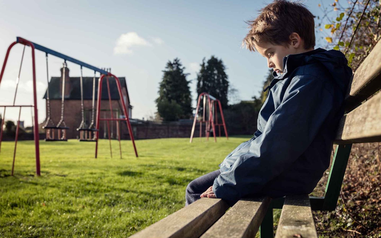 Child sitting on bench in the park, they look sad