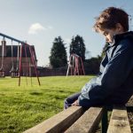 Child sitting on bench in the park, they look sad