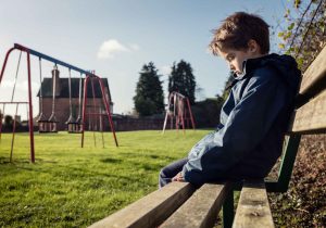 Child sitting on bench in the park, they look sad