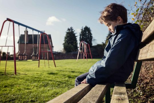 Child sitting on bench in the park, they look sad