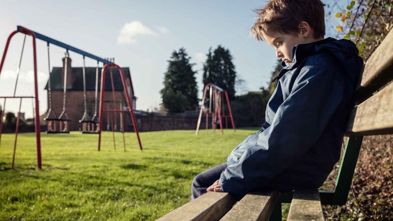 Child sitting on bench in the park, they look sad