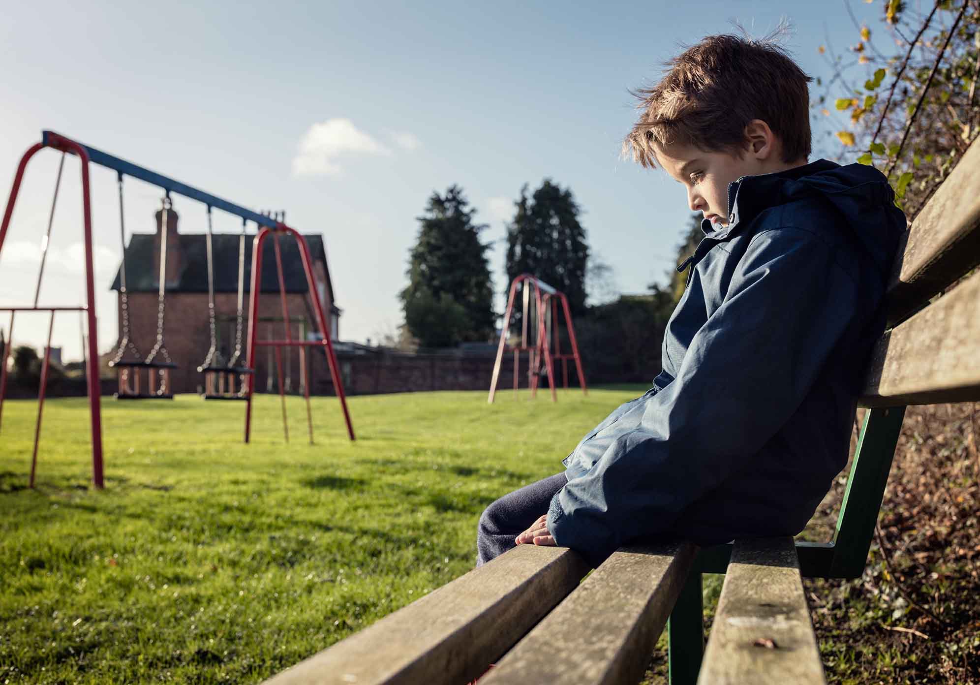 Child sitting on bench in the park, they look sad