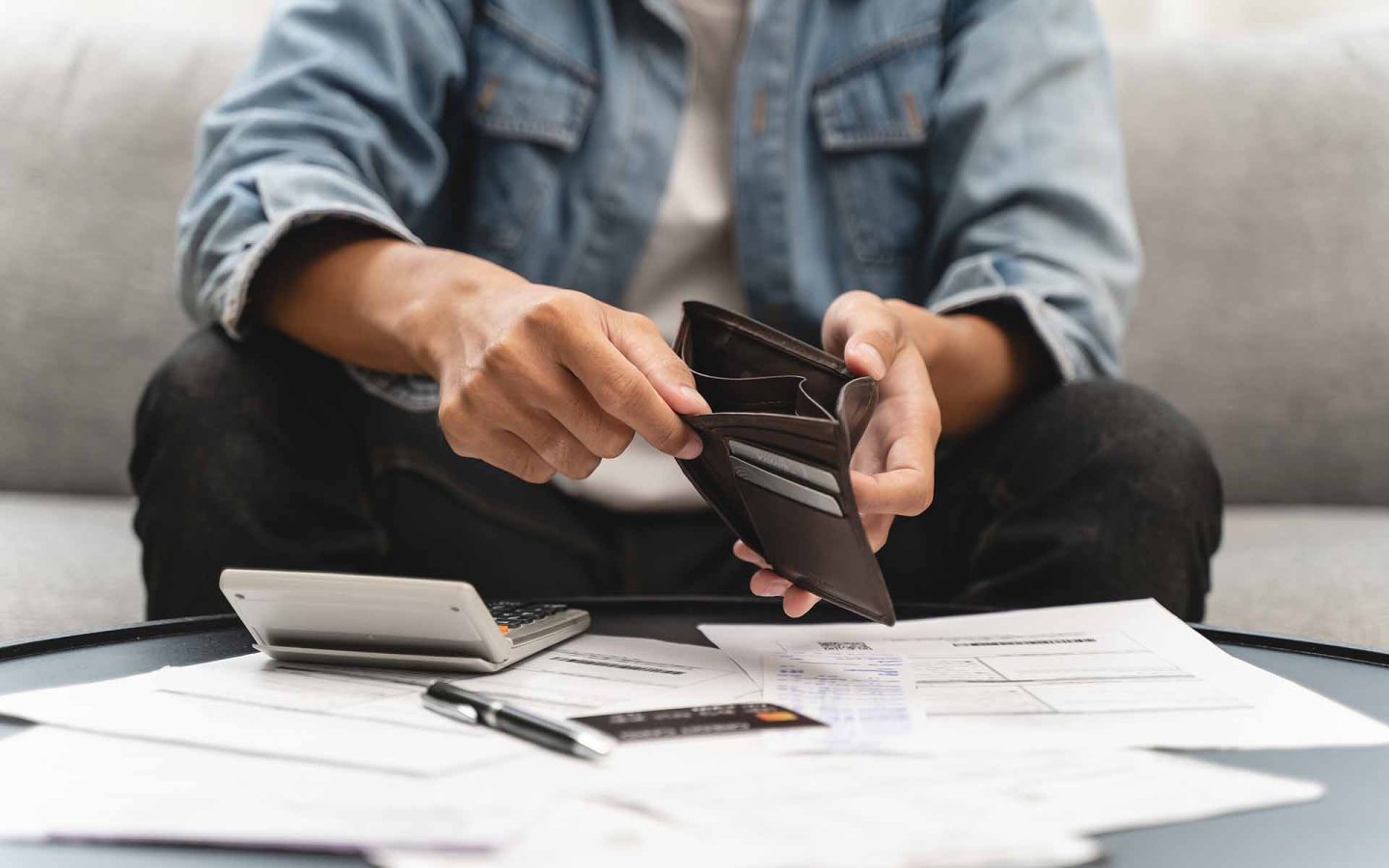 Person lookinng through empty wallet with calculator and paperwork on a table in front of them
