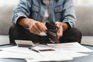 Person lookinng through empty wallet with calculator and paperwork on a table in front of them