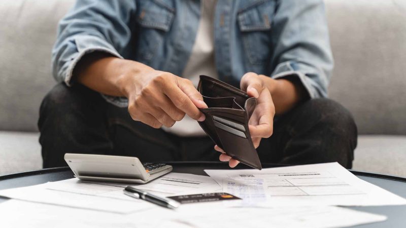 Person lookinng through empty wallet with calculator and paperwork on a table in front of them