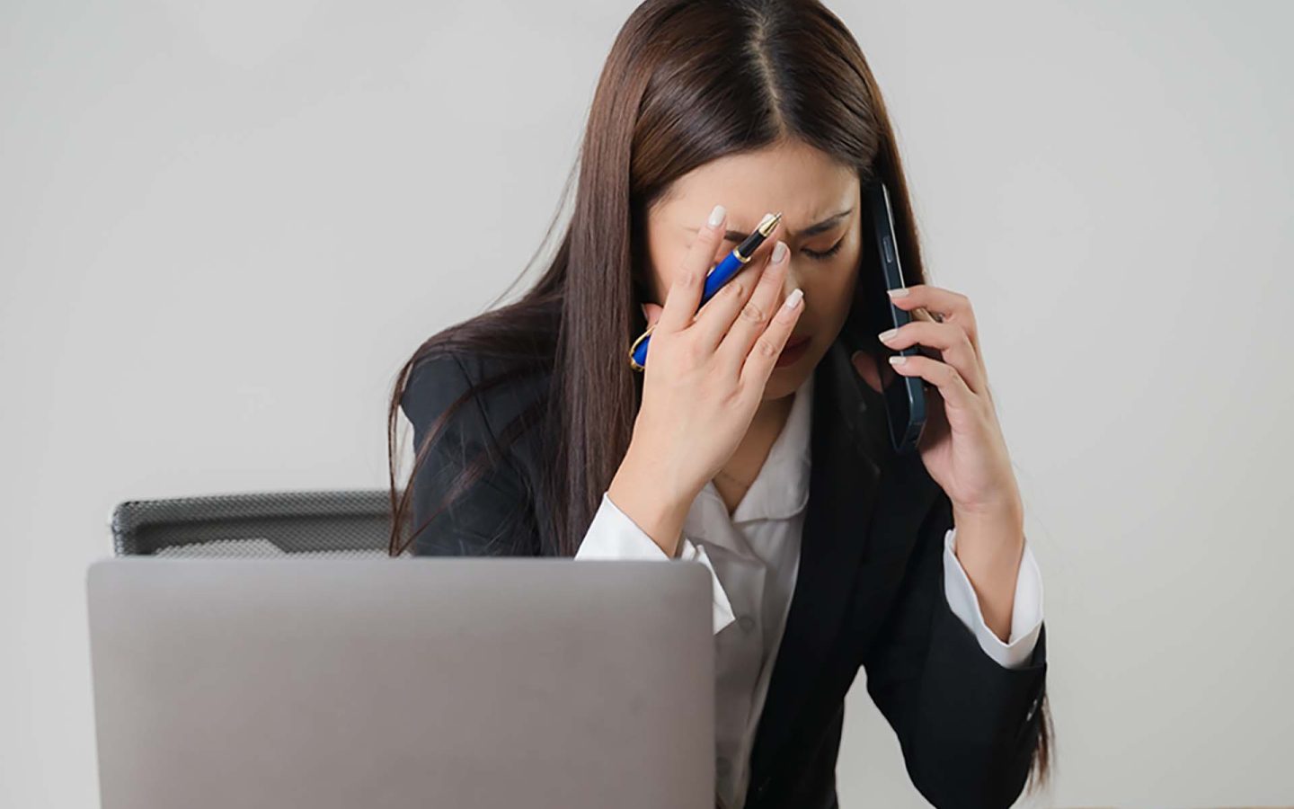 woman sitting at desk in front of laptop using mobile phone and looking worried